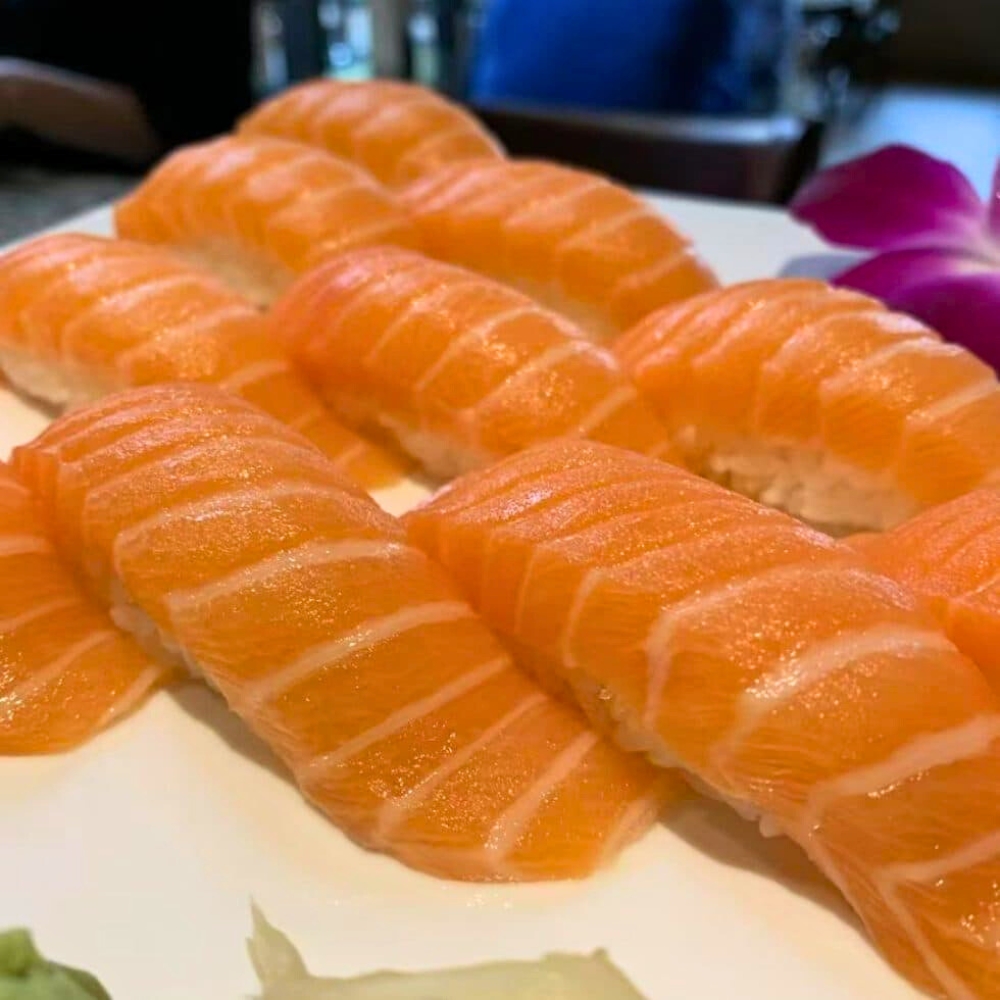 Neat rows of fresh salmon nigiri sushi on white plate