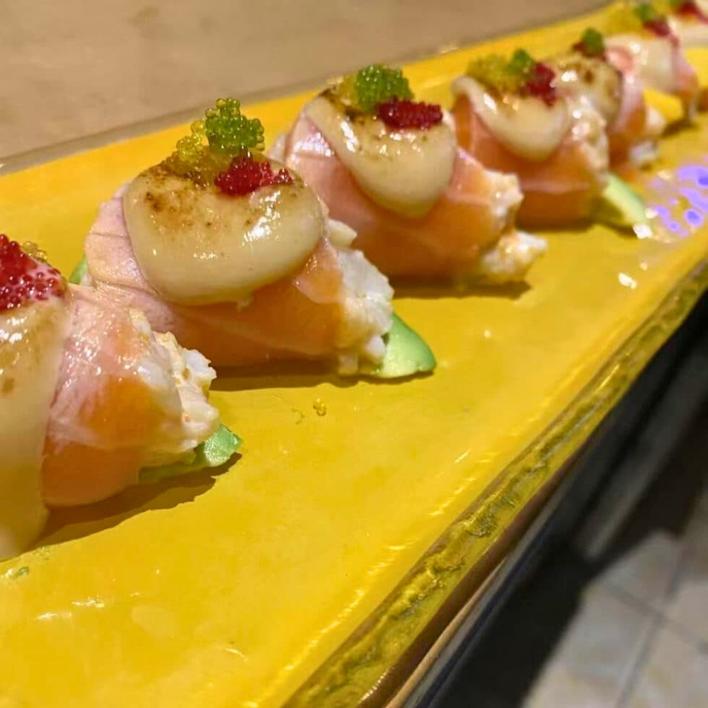 Salmon-wrapped sushi with scallops and tobiko on yellow plate