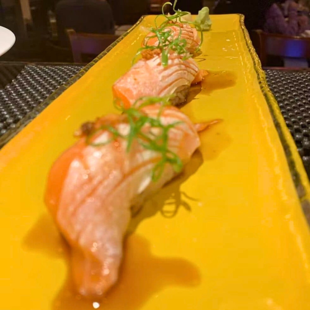 Seared salmon nigiri with sauce and green garnish