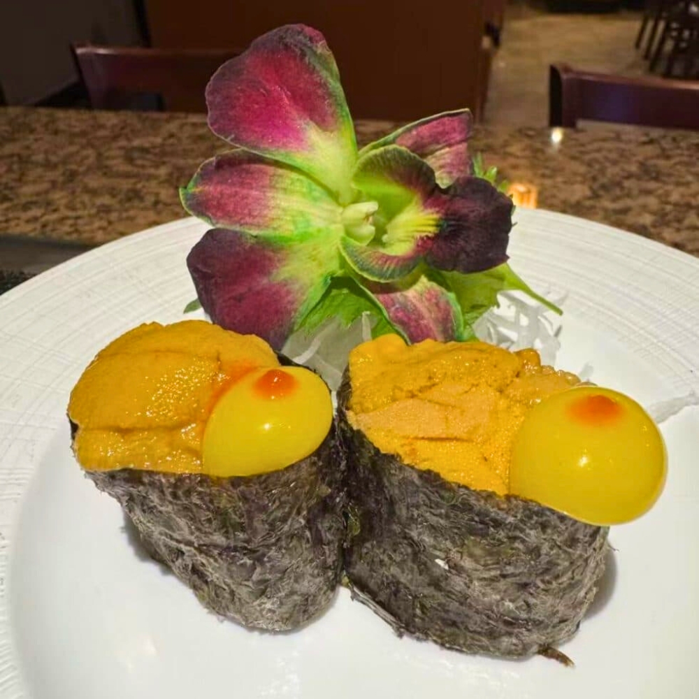 Uni gunkan maki with yellow garnish on white plate