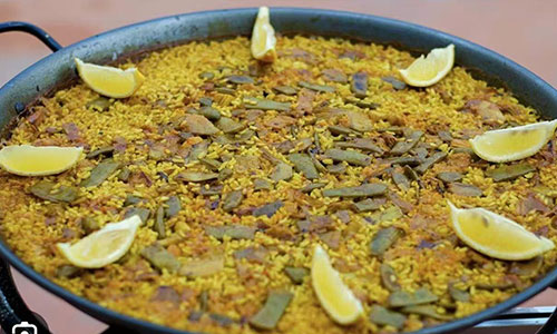 Classic vegetable paella in metal pan topped with fresh lemon wedges and green bean strips at La Paella, a Spanish Restaurant in Sugar Land