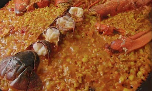 Lobster paella featuring split red lobster tails resting atop vibrant saffron-infused Spanish rice in metal pan at La Paella, a Spanish Restaurant in Sugar Land