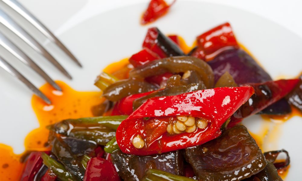 Spicy stir-fried eggplant with red chili peppers coated in glossy orange sauce on white plate at Papa Ma Fusion Food , an Chinese Cold Dish Restaurant in Flushing