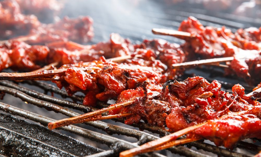Glazed marinated meat skewers smoking hot on metal barbecue grill grates at Papa Ma Fusion Food , an Chinese Cold Dish Restaurant in Flushing