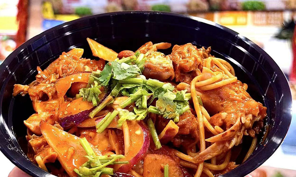 Single black takeout bowl of braised chicken cold noodles tossed with red onion, potato and fresh cilantro in spicy sauce at Papa Ma Fusion Food , a Chinese Cold Dish Restaurant in Flushing