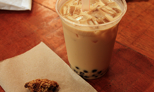 Iced boba milk tea with a cookie on the side at Poke House Huntington, a Hawaiian restaurant in Huntington