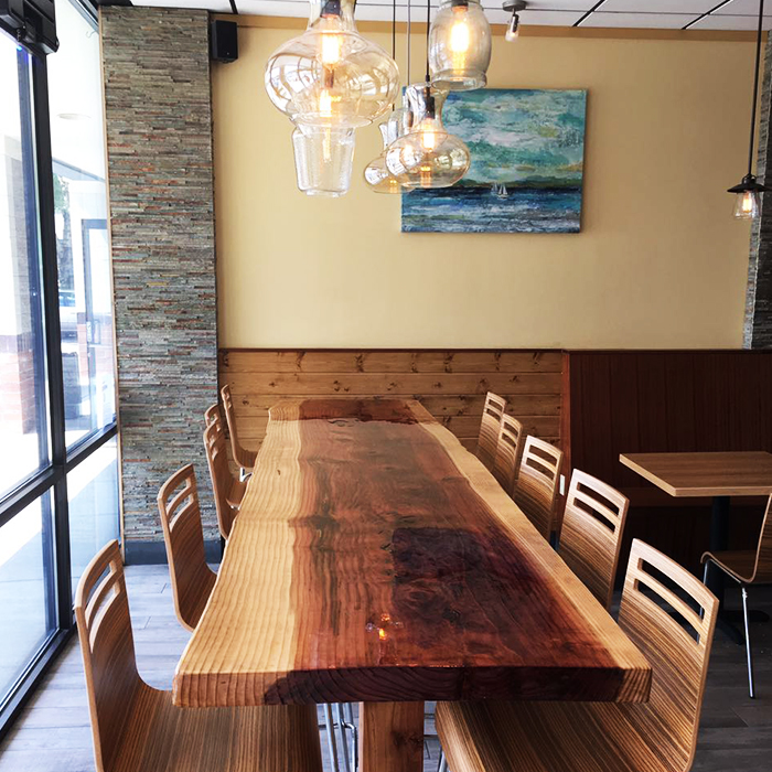 Restaurant interior with wooden plank wall featuring Poke Makana logo and light wood dining tables at Poke Makana, a Hawaiian restaurant in Sherwood