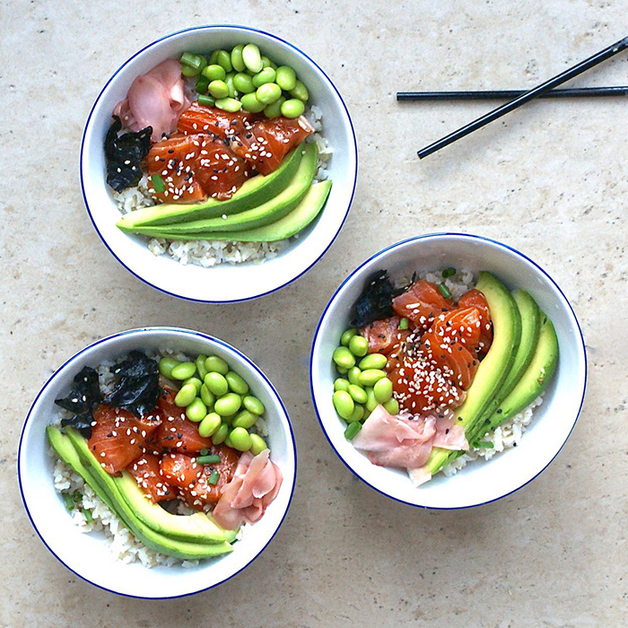 Three salmon poke bowls with avocado, edamame, pickled ginger, and seaweed garnish on a light stone surface at Poke Makana, a Hawaiian restaurant in Sherwood