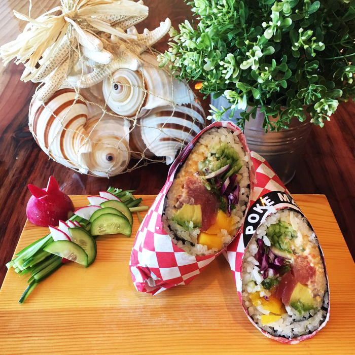 Two poke burritos wrapped in checkered paper, served with fresh veggie garnish and coastal decor at Poke Makana, a Hawaiian restaurant in Sherwood
