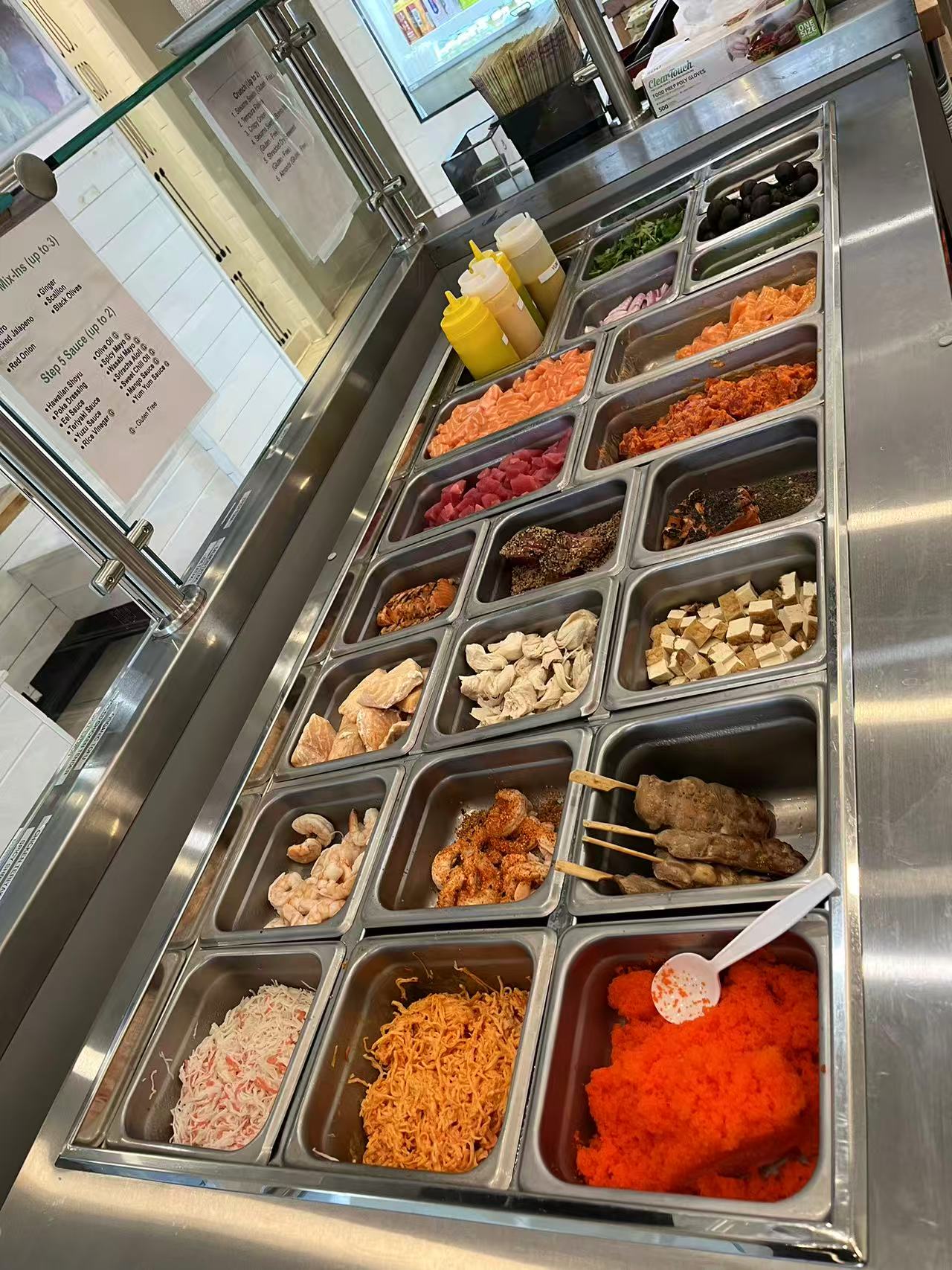 Poke-One-Poke-Bowl-Restaurant-Morris-Plains Poke bowl bar with fresh seafood, tofu, and toppings in stainless steel trays.