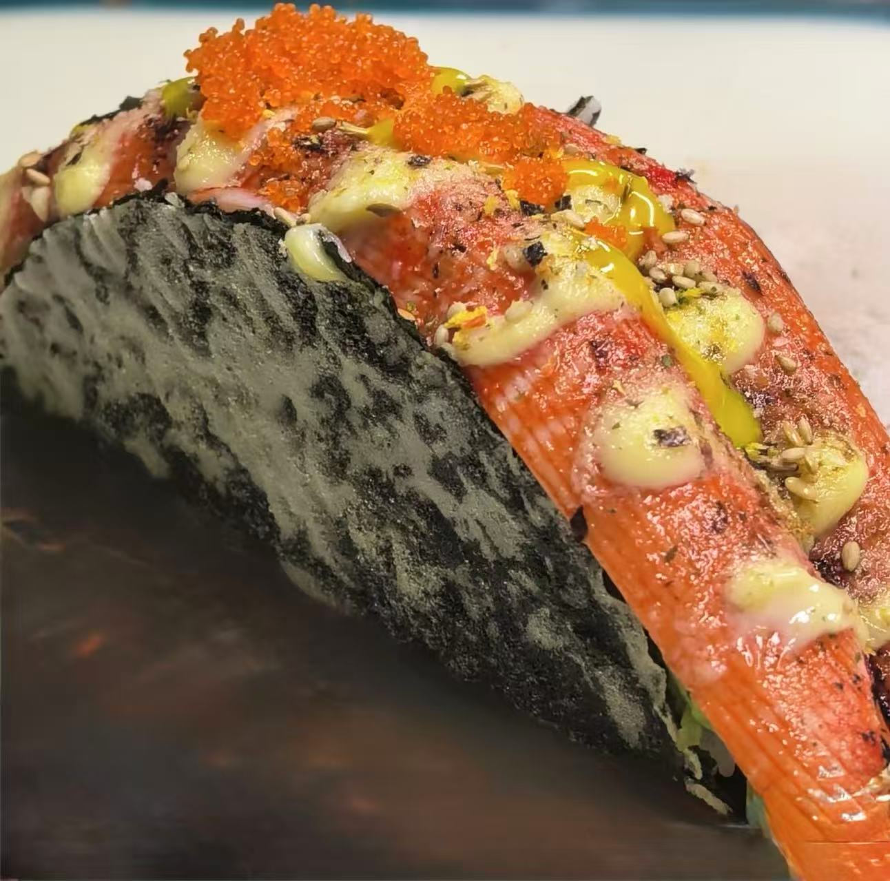 Close-up of a sushi taco with crab, tobiko, sauces, and seaweed shell.