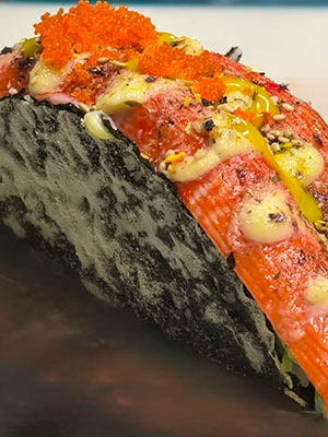 Close-up of a sushi taco with crab, tobiko, sauces, and seaweed shell.