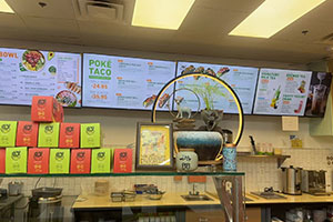 Poke Taco restaurant counter with digital menu boards and branded takeout boxes.