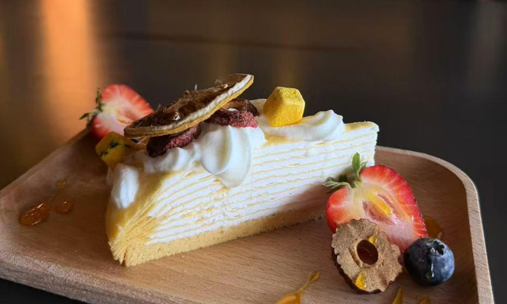 Yellow mille crepe cake slice with cream, dried citrus and strawberry garnish at Pop Ice Cream, a Dessert Shop restaurant in Bonita Springs