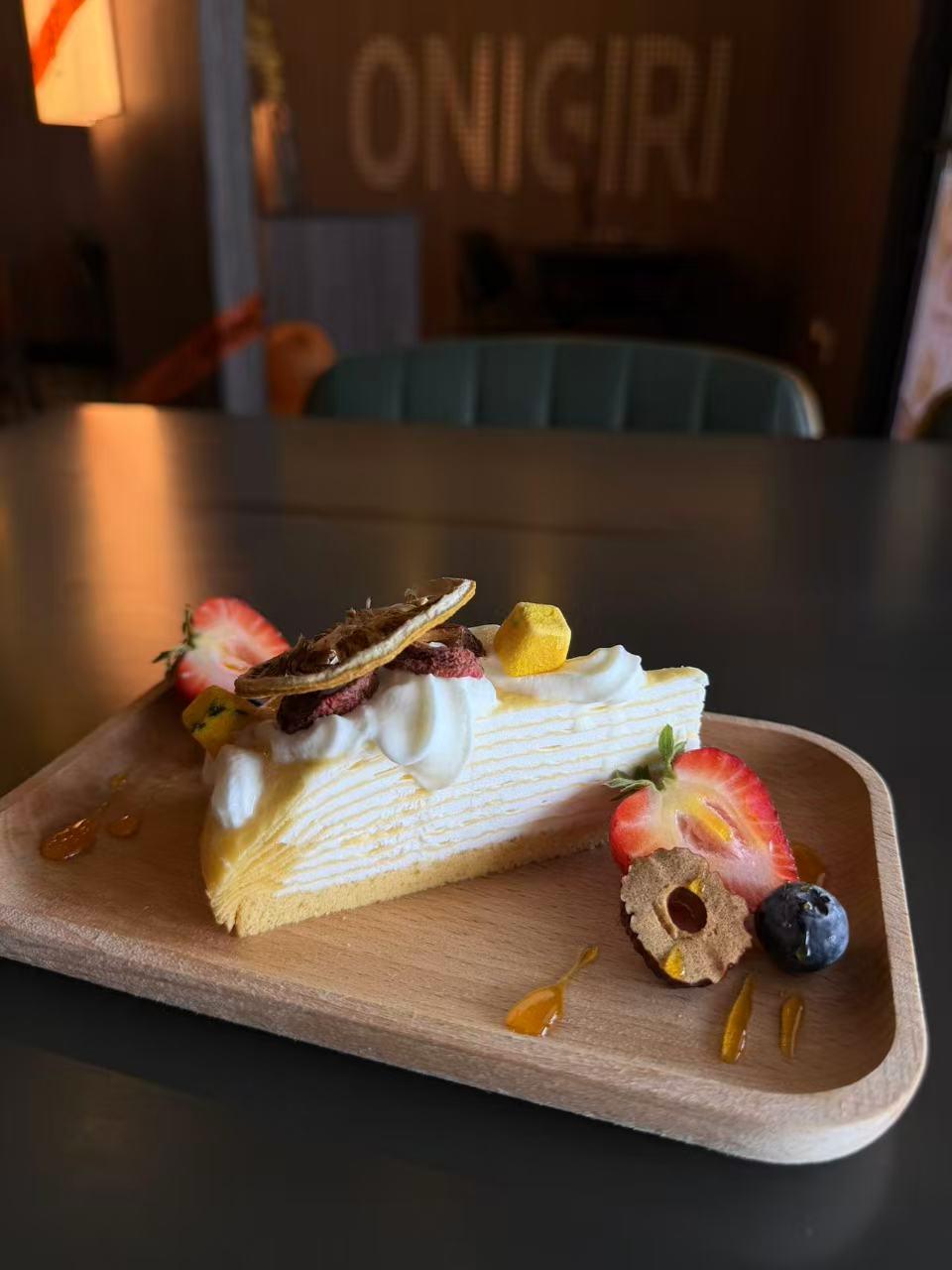 Layered crepe cake topped with fresh strawberry, blueberry and candied citrus on wooden plate at Pop Ice Cream, a Dessert Shop in Bonita Springs