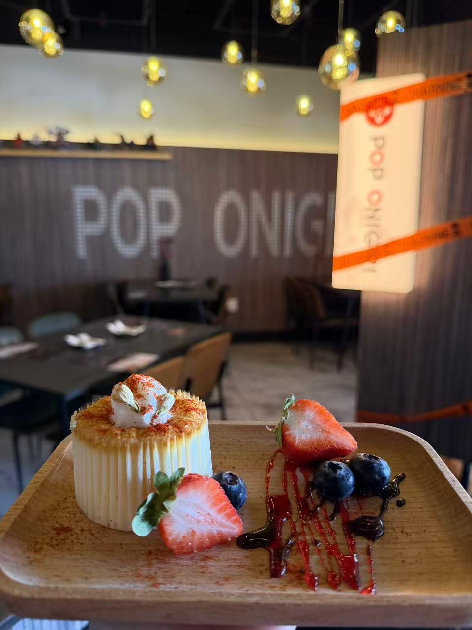 Torched creamy cheesecake garnished with berries and berry syrup on wooden tray inside dining space at Pop Ice Cream, a Dessert Shop in Bonita Springs