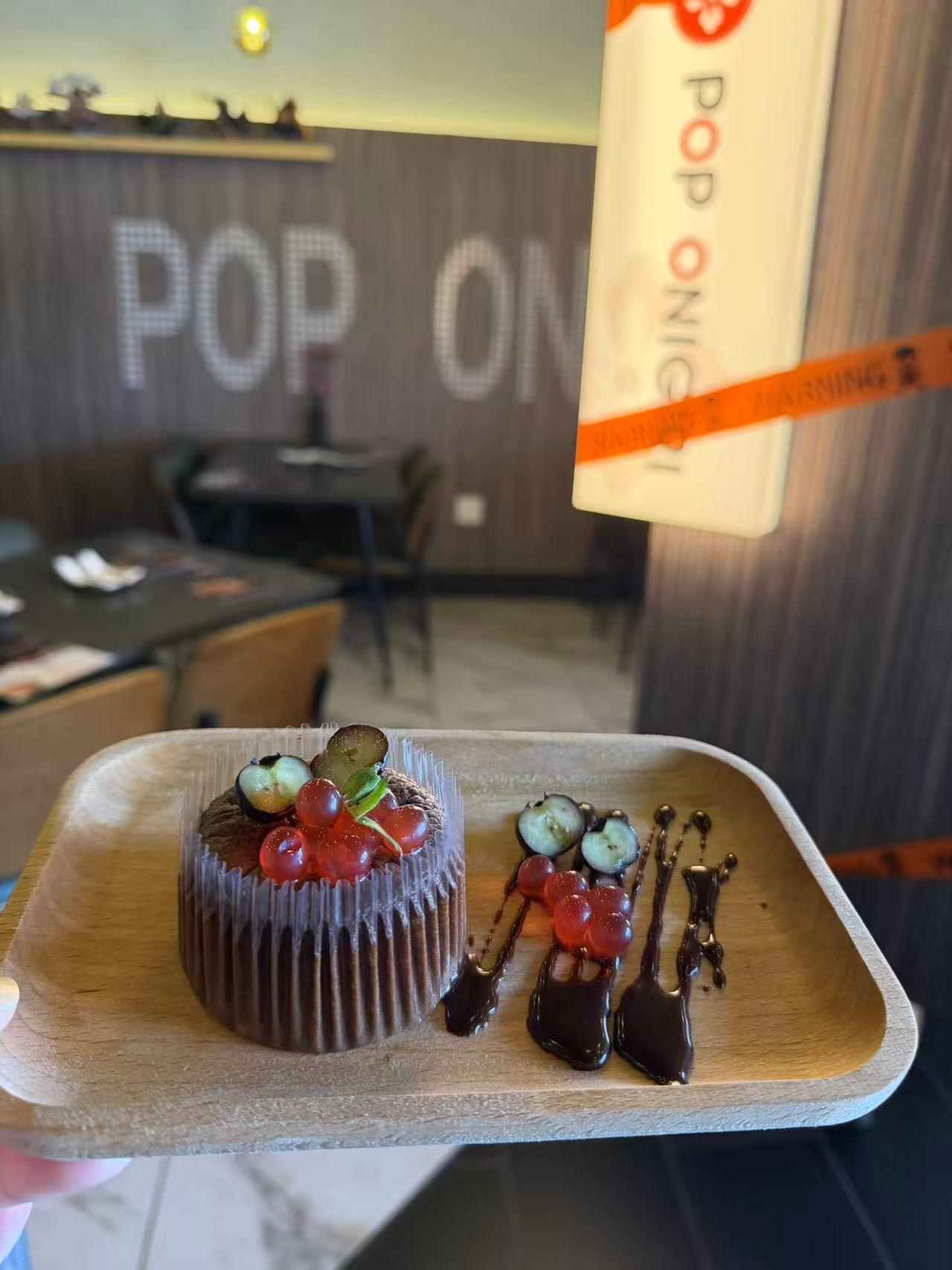 Rich chocolate cupcake topped with red currants and chocolate drizzle on natural wood serving tray at Pop Ice Cream, a Dessert Shop in Bonita Springs