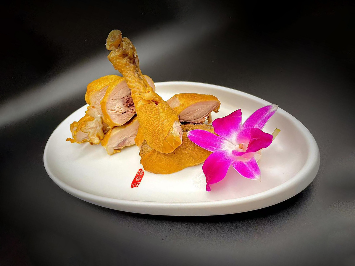 Sliced salted chicken garnished with a pink orchid on a white plate at Precious, a Chinese Restaurant in Austin
