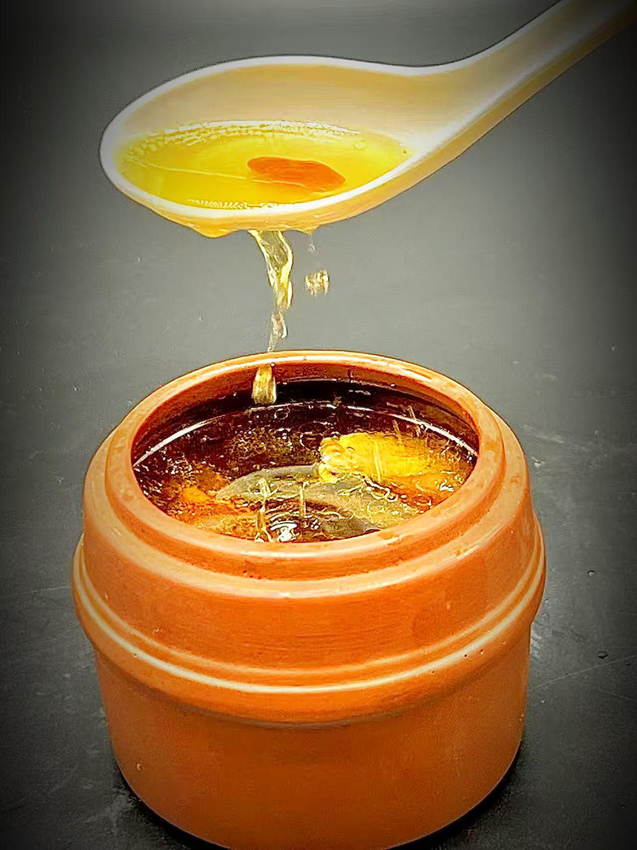 Warm nourishing Chinese herbal soup pouring from a spoon into a clay pot at Precious, a Chinese Restaurant in Austin