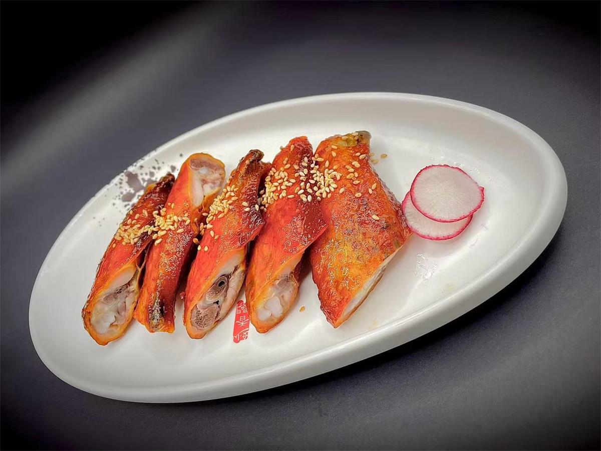 Roasted chicken wings with sesame seeds and radish slices on a white plate at Precious, a Chinese Restaurant in Austin