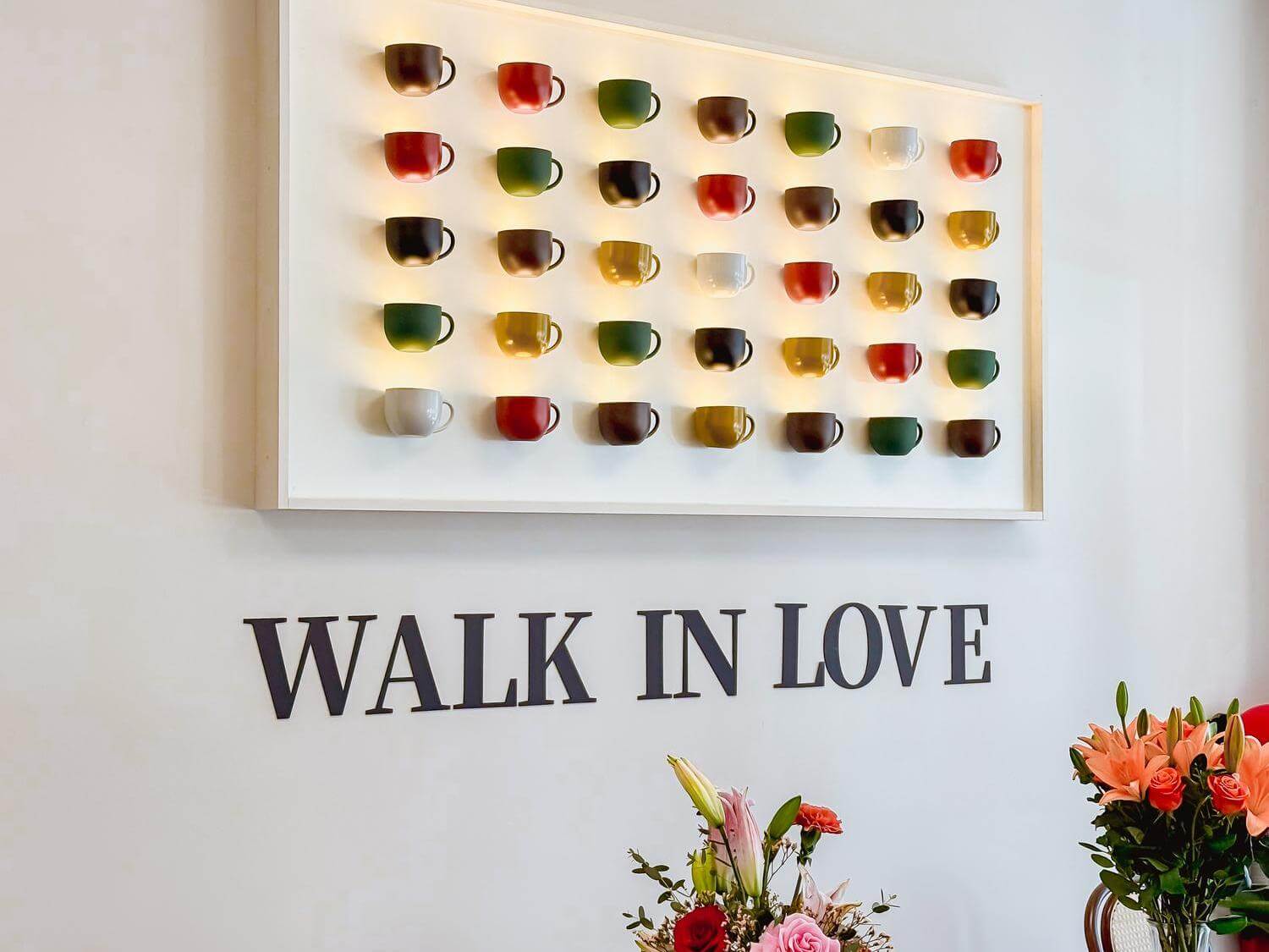 Wall decor with colorful cups and "WALK IN LOVE" sign at Bliss Café, a Coffee Shop in Oviedo