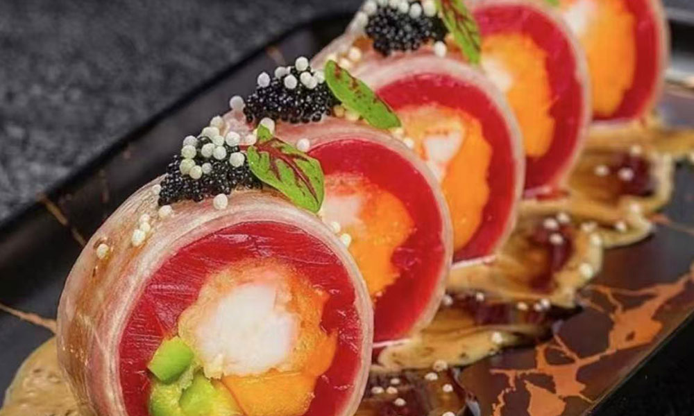 Wrapped tuna sashimi roll filled with avocado and scallop, topped with caviar and microgreens on dark plate at Quan Izumi , an Japanese Restaurant in Centereach