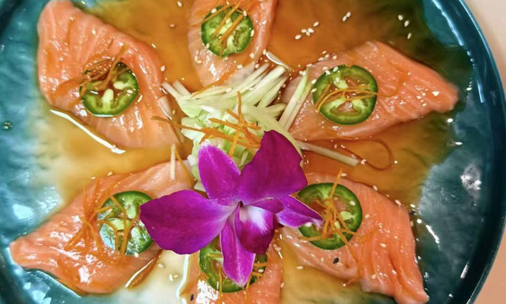 Marinated salmon sashimi garnished with jalapeño, ginger and purple orchid flower on teal ceramic plate at Quan Izumi , an Japanese Restaurant in Centereach