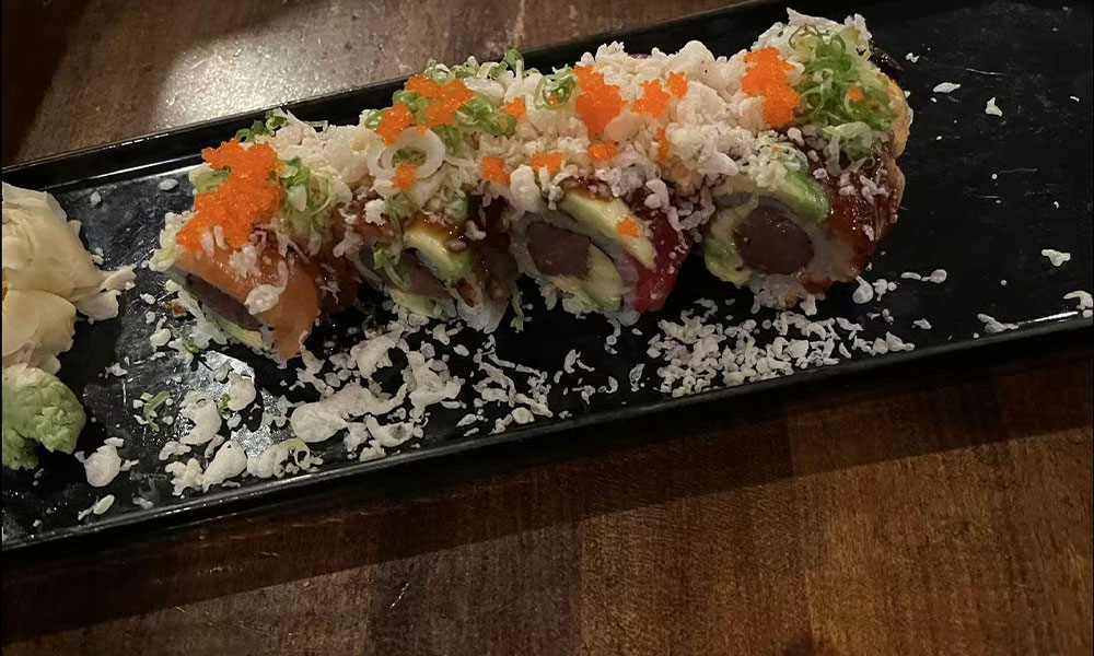 Colorful sushi roll topped with tobiko, crispy flakes and green onion served with ginger and wasabi on black tray at Quan Izumi , an Japanese Restaurant in Centereach