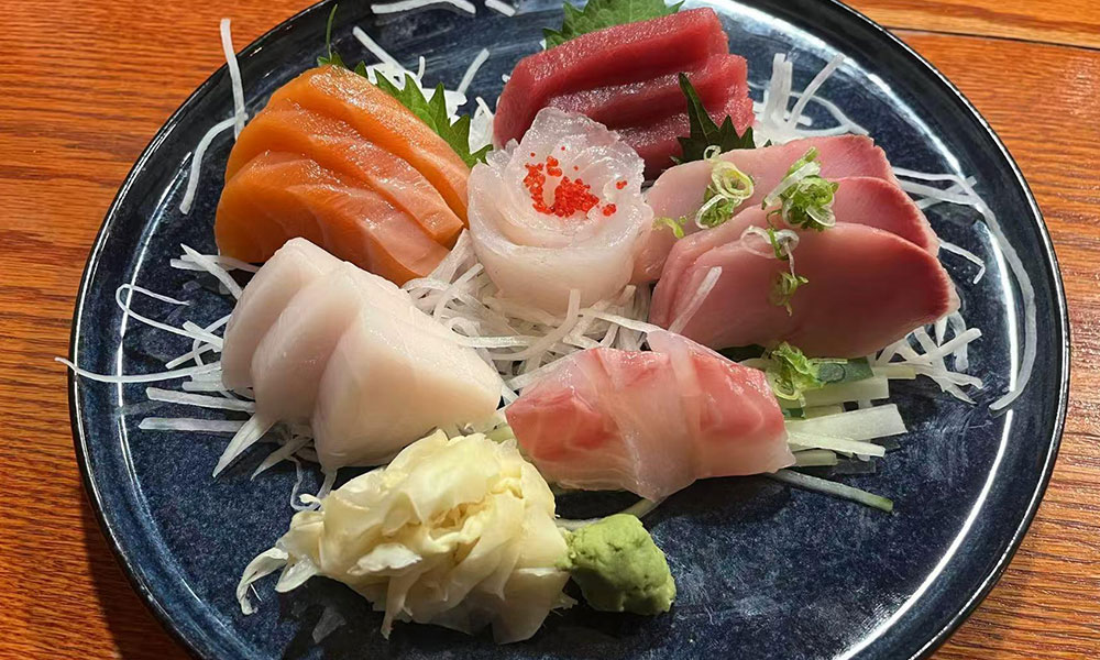 Mixed fresh sashimi varieties arranged with daikon radish, pickled ginger and wasabi on dark blue round plate at Quan Izumi , an Japanese Restaurant in Centereach