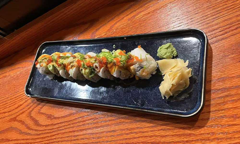 Seafood sushi roll drizzled with spicy sauce, garnished with tobiko, ginger and wasabi on dark rectangular ceramic plate at Quan Izumi , an Japanese Restaurant in Centereach