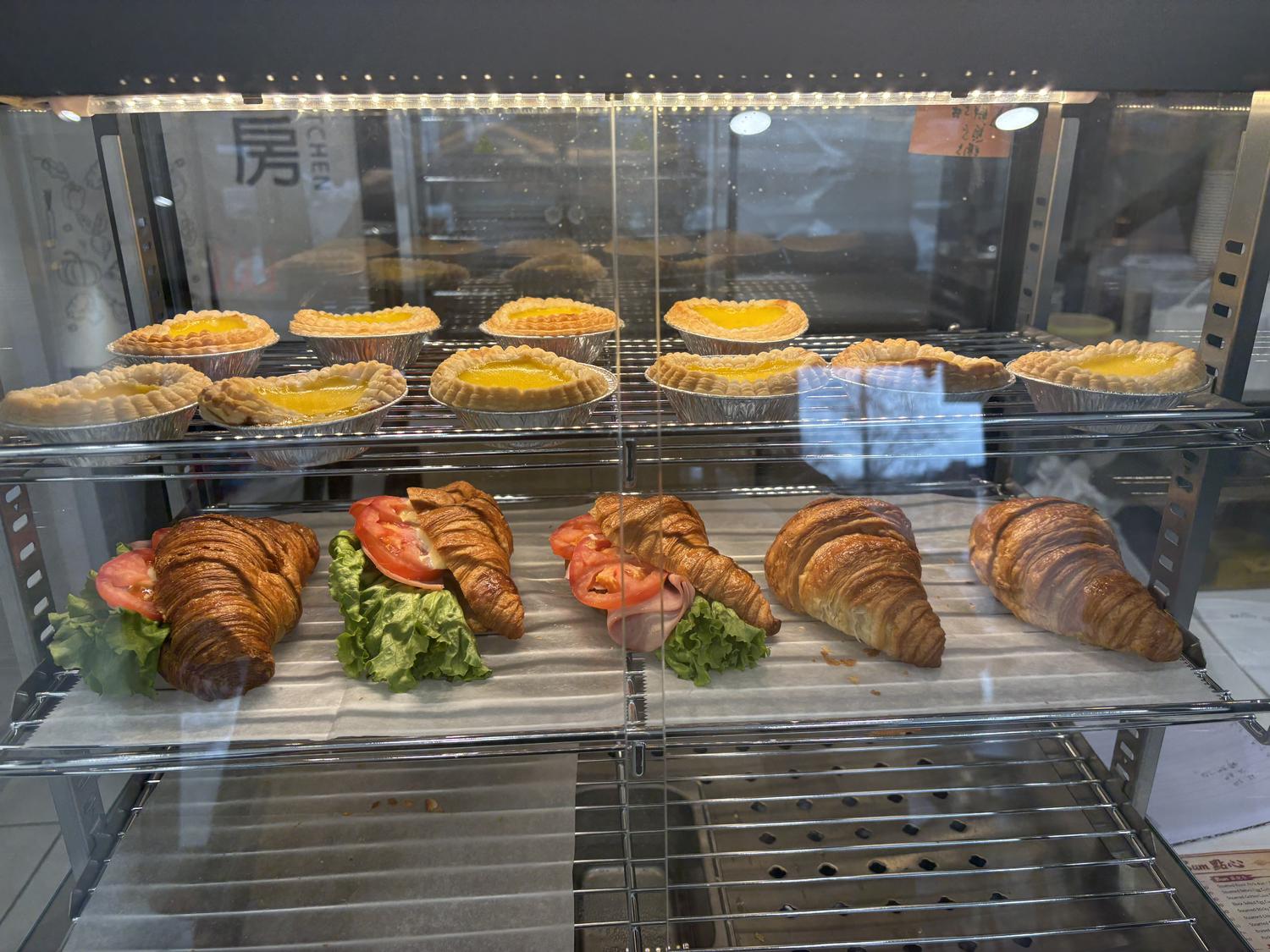 Egg tarts and croissants in a glass display case at Rainbow 1 Bakery, a Bakery in Brooklyn