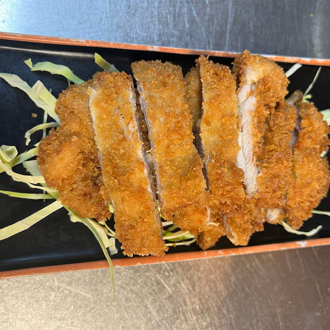 Crispy sliced fried pork katsu served on dark rectangular plate with shredded cabbage