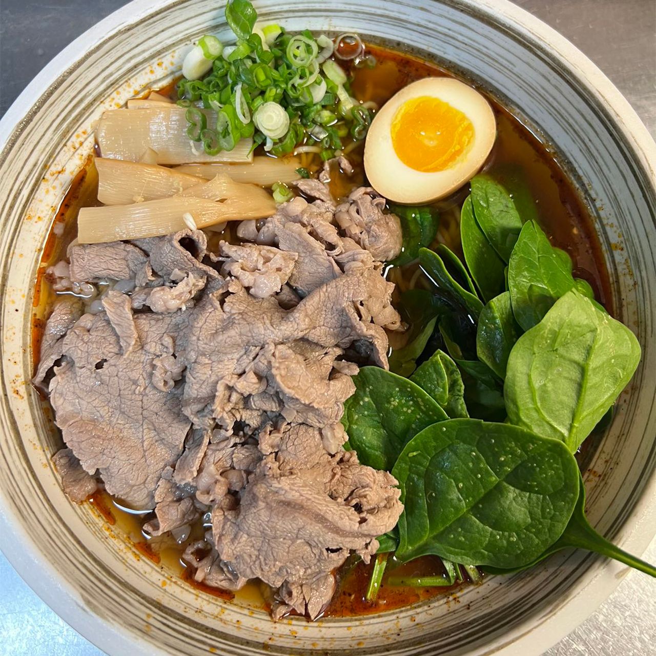 Spicy beef ramen with sliced beef, spinach, bamboo shoots, green onion and soft egg