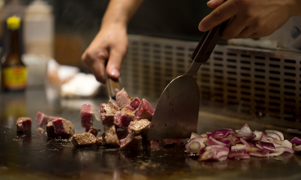 Chef cooking steak on a teppanyaki grill with onions at Red Door Asian Bistro & Hibachi, an Asian Restaurant in Fort Lauderdale