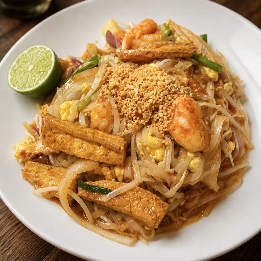 Pad Thai with tofu, shrimp, peanuts, and a lime wedge on a white plate