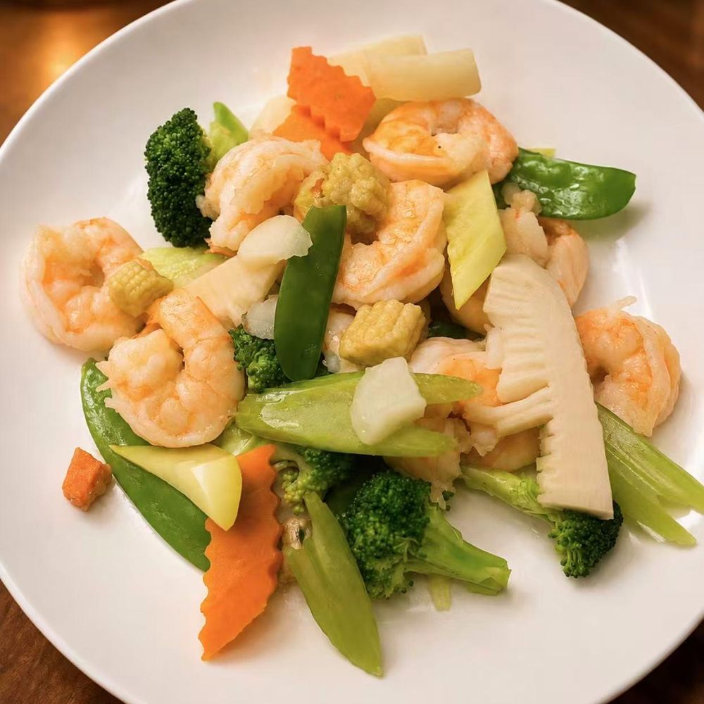 Stir-fried shrimp with broccoli, snow peas, and baby corn on a white plate Stir-fried shrimp with broccoli, snow peas, and baby corn on a white plate