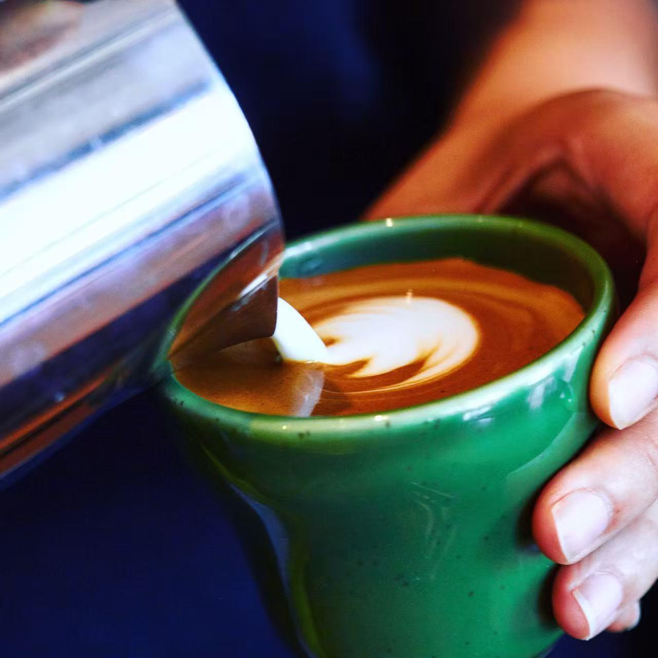 Barista pouring latte art into a green mug at Rise & Grind Cafe, a Coffee Shop in Los Angeles