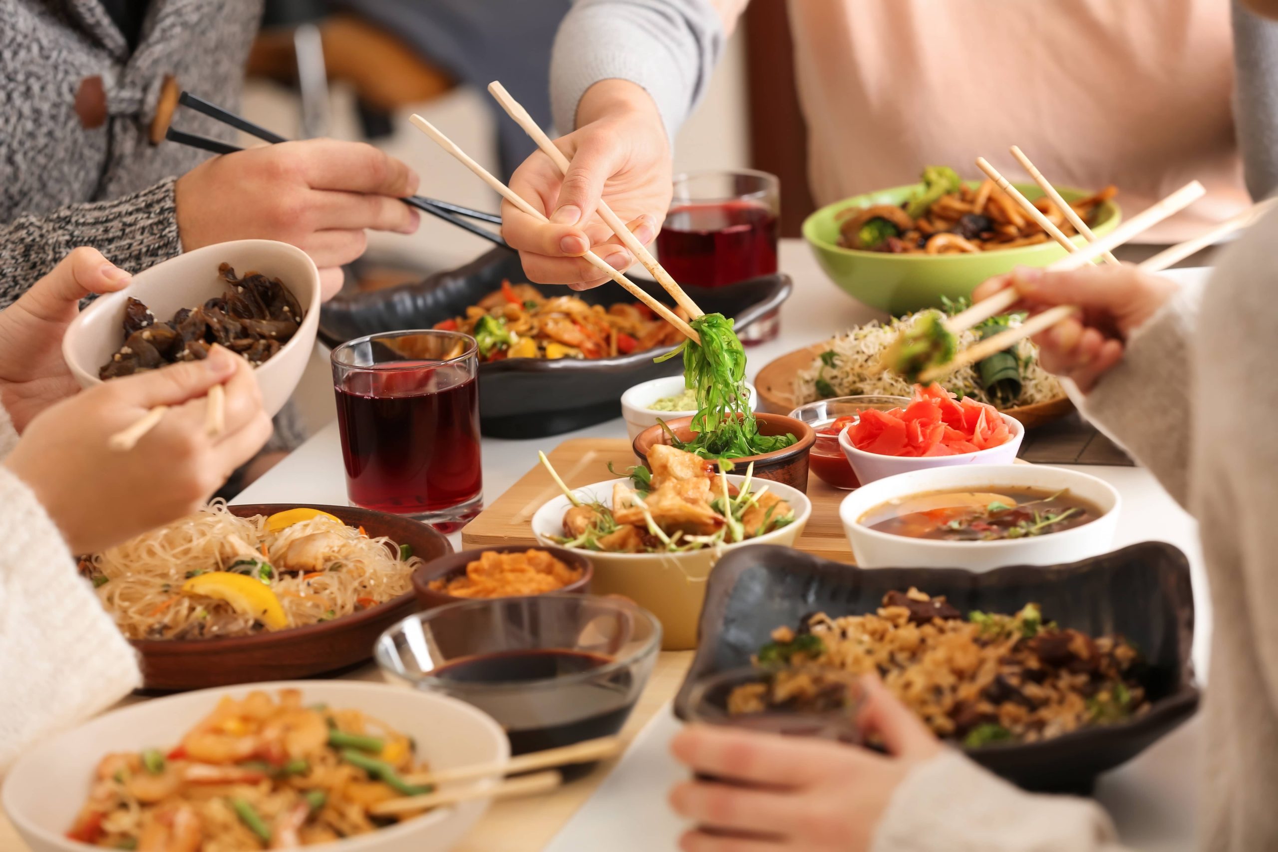 Family and Friends Sharing an Asian Meal with Chopsticks Around a Table Filled with Traditional Dishes and Soups