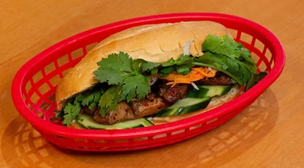 Grilled pork banh mi sandwich filled with cucumber, cilantro and pickled veggies in red plastic basket at Saigon #1, a Vietnamese restaurant in Virginia Beach