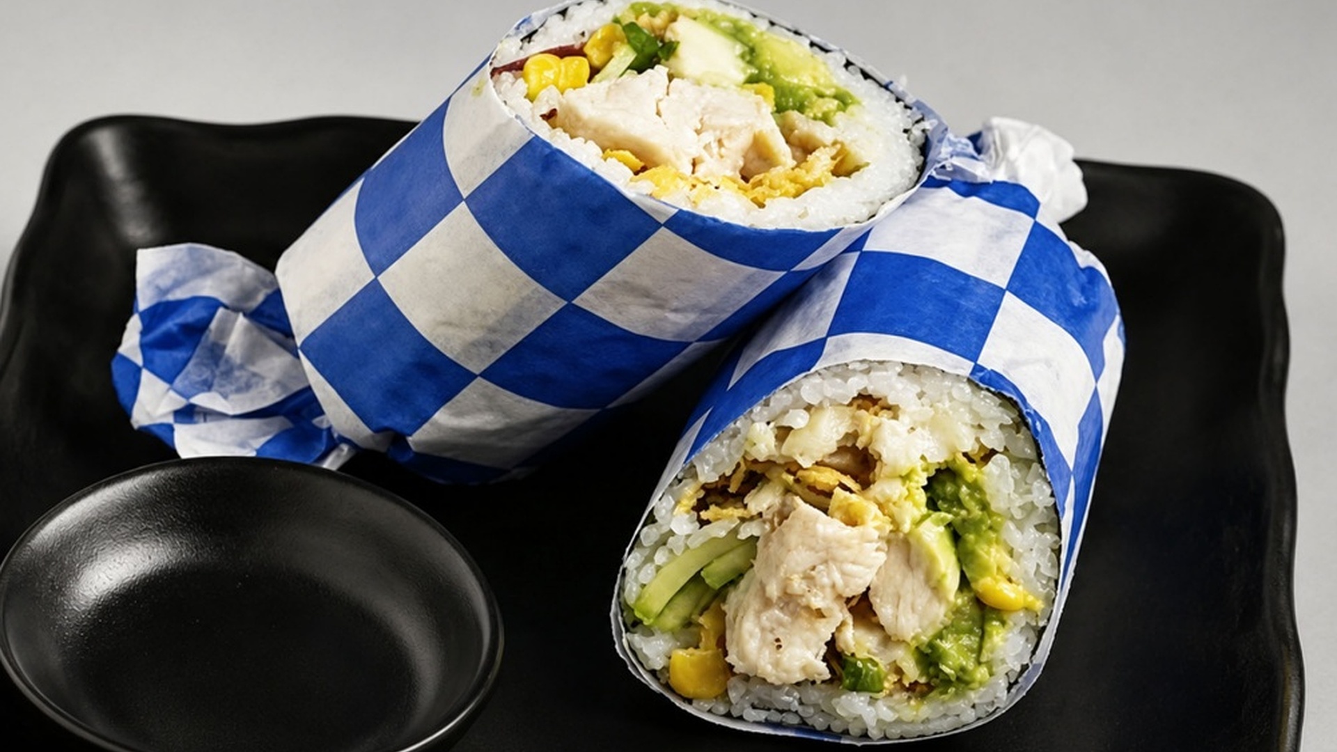 Chicken avocado sushi burrito wrapped in checkered paper at Sakana Western, a Hawaiian Restaurant in Chicago