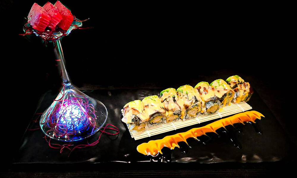 Gourmet sushi roll platter with glowing glass decor and creamy orange sauce drizzle at Saki, a Sushi Restaurant in Clear Water