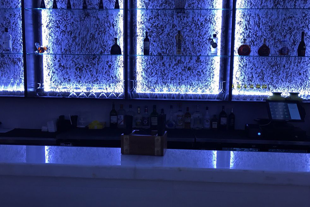 Bar counter with illuminated shelves and various bottles at Sasa, a Japanese Restaurant in Farmingdale.