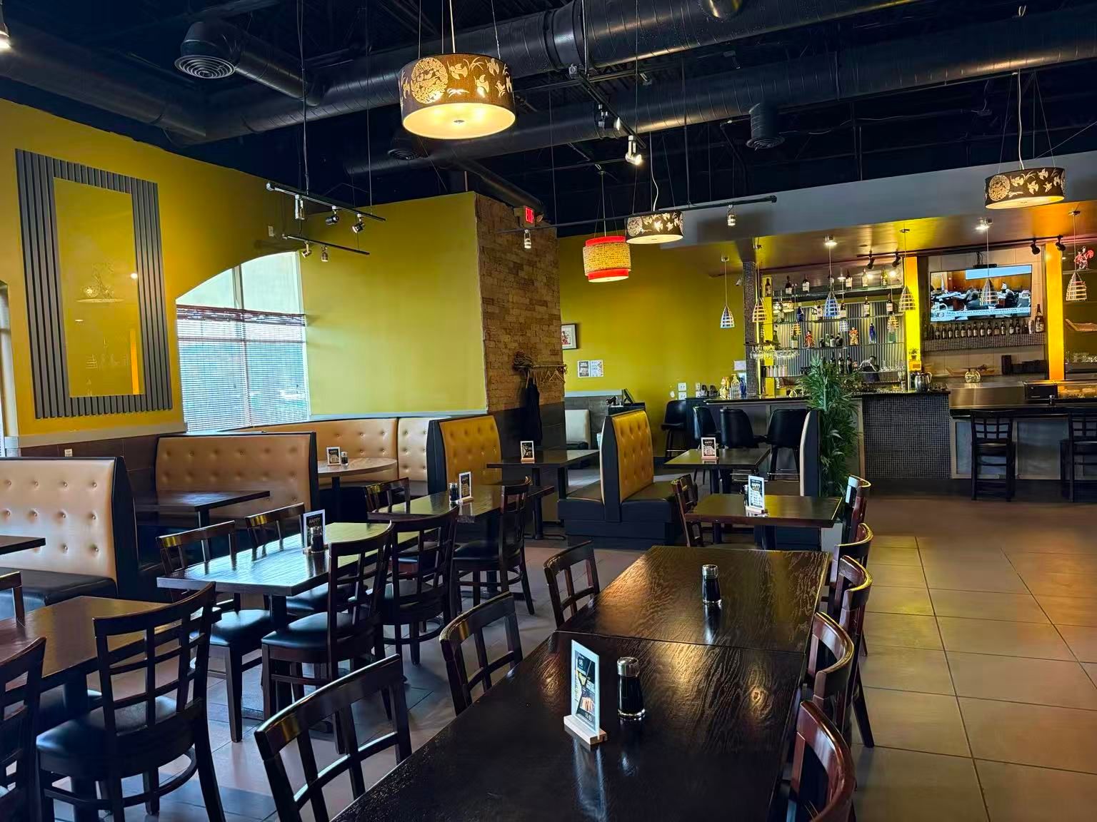 Bright yellow dining room with booth seating, wooden tables and hanging decorative lamps