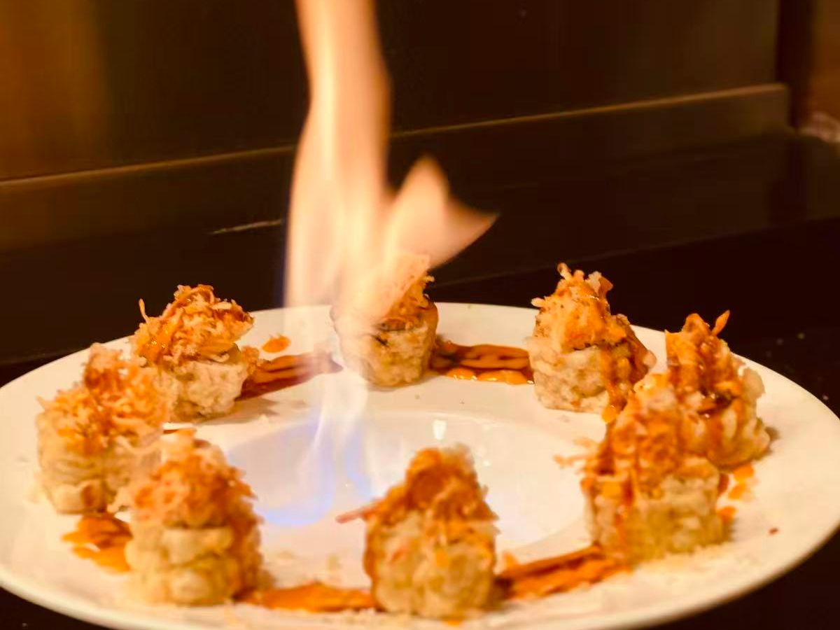 Flaming sushi rolls on white plate with crispy toppings and drizzled brown sauce