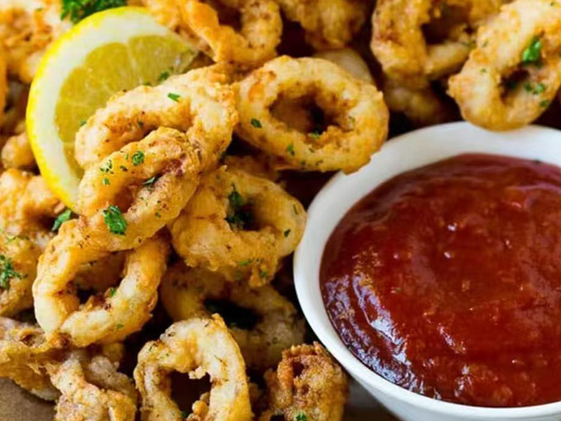 Golden fried calamari rings with lemon wedge, parsley and spicy red dipping sauce at Seafood&wings, a Seafood Restaurant in Greenville