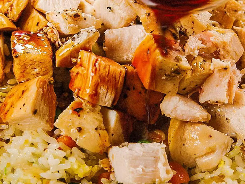 Grilled chicken cubes being drizzled with sauce over fried rice and mixed veggies at Seafood&wings, a Seafood Restaurant in Greenville