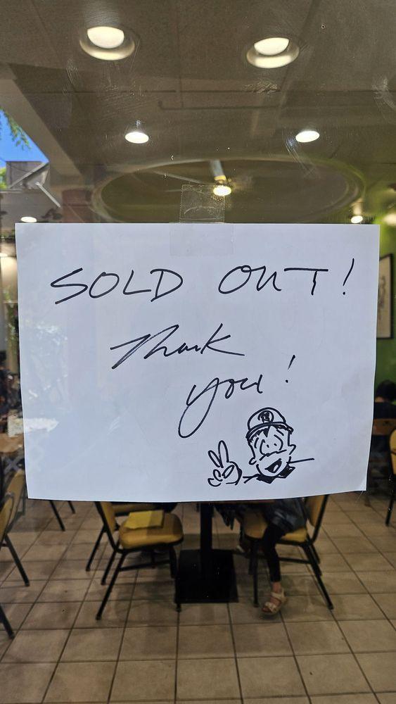 Seasons-Taiwanese-Eatery-Taiwanese-Restaurant-Sold-Out-Thank-You-Notice-Honolulu White notice on glass door with handwritten black text 'SOLD OUT! Thank you!', cartoon character with hat making peace sign at bottom right, restaurant tables visible in background at Seasons Taiwanese Eatery,a Taiwanese Restaurant in Honolulu