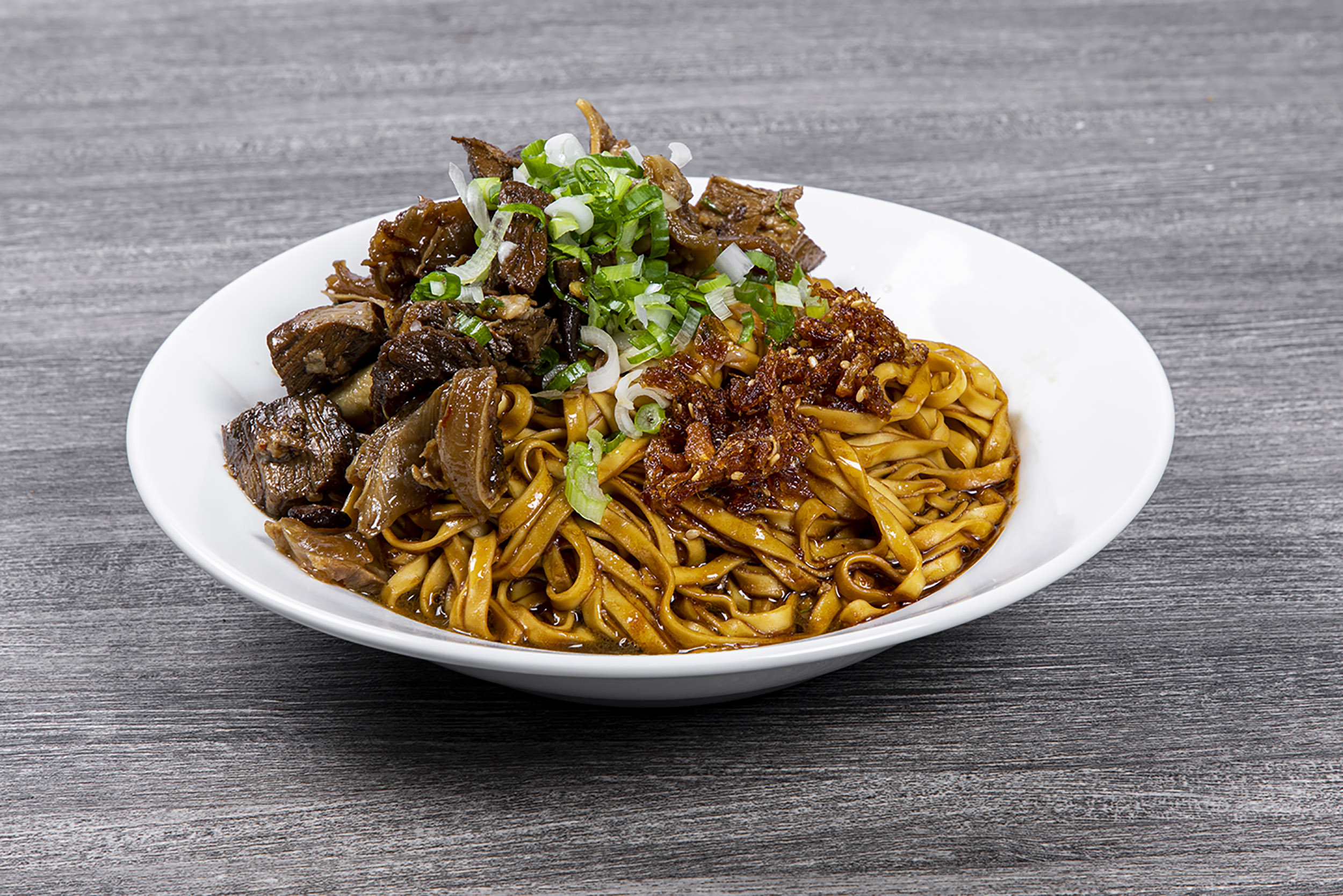 Braised beef wide dry noodles topped with green onion and chili crisp at Shaxian Snacks, a Chinese Restaurant in Elmhurst