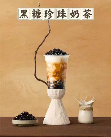 Brown sugar boba milk tea served in cup on white pedestal, topped with black tapioca pearls. Extra pearls on dish, small milk jar beside, Chinese title at top.