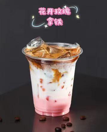 Layered iced rose latte in clear plastic cup, pink base, milk and espresso with ice cubes. Coffee beans scattered on dark table, Chinese title above.